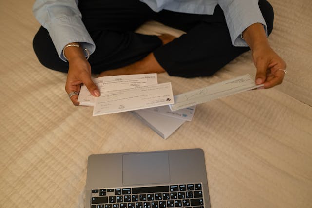 Person holding cheques in their hands with a laptop sitting infront of them